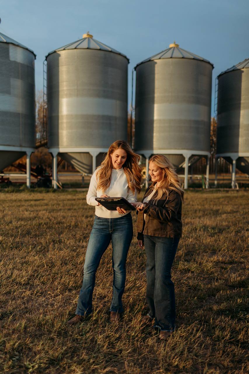 Two women reviewing a tablet together in front of metal grain bins.